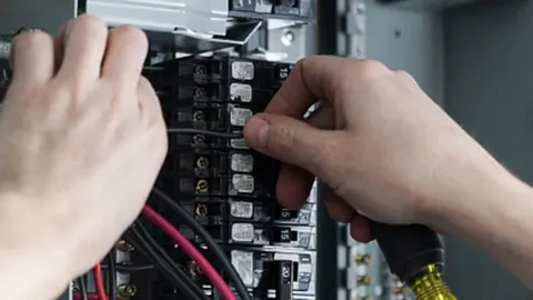 An electrician working on an outdoor box to upgrade an electrical panel for a building.