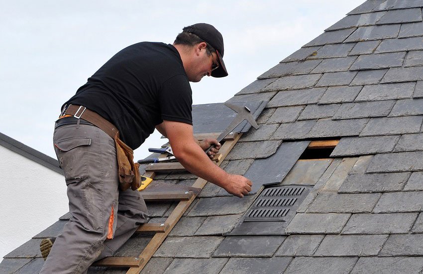 A man works on a roof using a ladder, representing local roofing services in action.