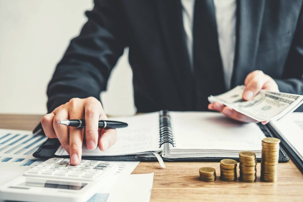 Businessman's hand counting cash on a desk, with a calculator nearby, illustrating money management practices.