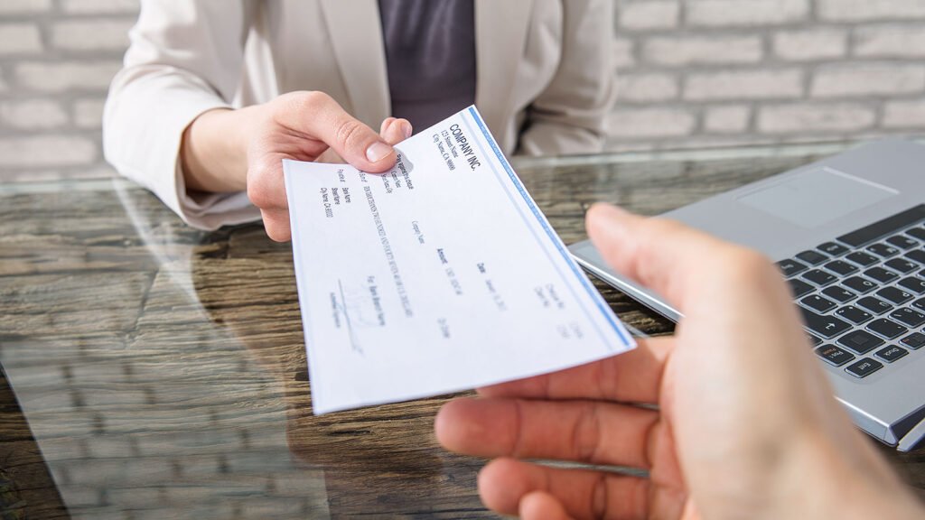 A person hands a check to another at a desk, illustrating the concept of paycheck optimization.
