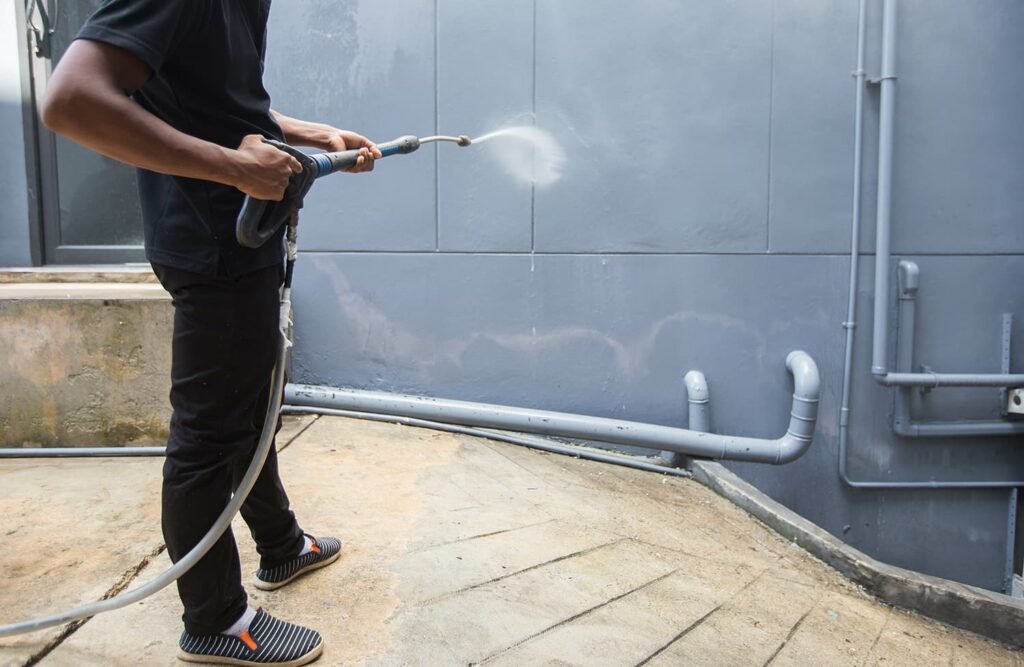 A professional technician using a high-pressure washer to power wash house exterior walls and remove dirt