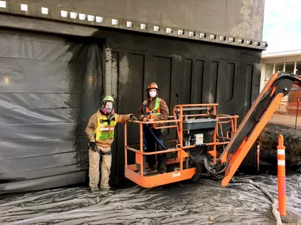 Worker using mobile sandblasting equipment on an industrial job site.