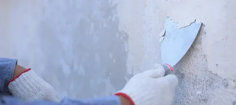 Surface preparation and paint removal service showing old peeling paint being scraped off a wall.