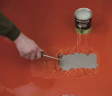 Hand using a scraping tool for professional paint removal on a damaged wall before repainting.